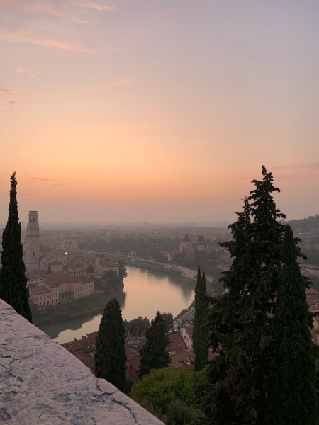 View of Verona, with the river, colorful sky, trees, and red roofed buildings.